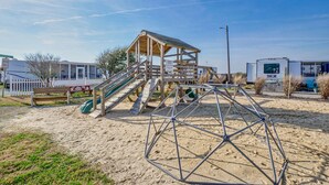 Een strand speeltuin met een houten huisje, glijbanen en een zandbak.