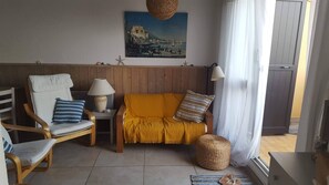 A cozy living room with a wooden panel wall, a sofa, a chair, a lamp, and a painting of a coastal scene. - Absolute beach front apartment Plage Roquille Fabulous Views Direct beach access (Agde,)