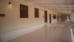 A corridor with wooden doors and light fixtures on the wall. - Dariya mahal Gopnath (Talaja)