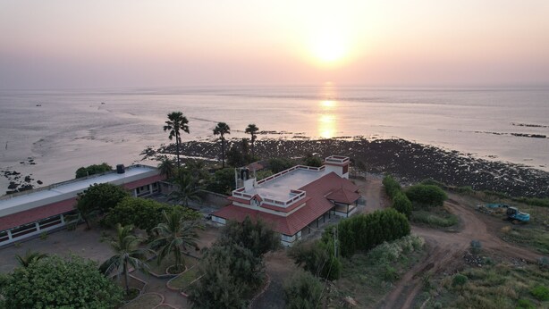 An aerial view of a coastal property with a building featuring a red roof, surrounded by greenery and a dirt path. - Dariya mahal Gopnath (Talaja)