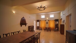 A spacious dining area with a long wooden table and chairs, a chandelier, and a bookshelf. - Dariya mahal Gopnath (Talaja)