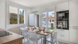 Une cuisine moderne avec des meubles blancs, une table à manger en bois et une vue sur l’extérieur.