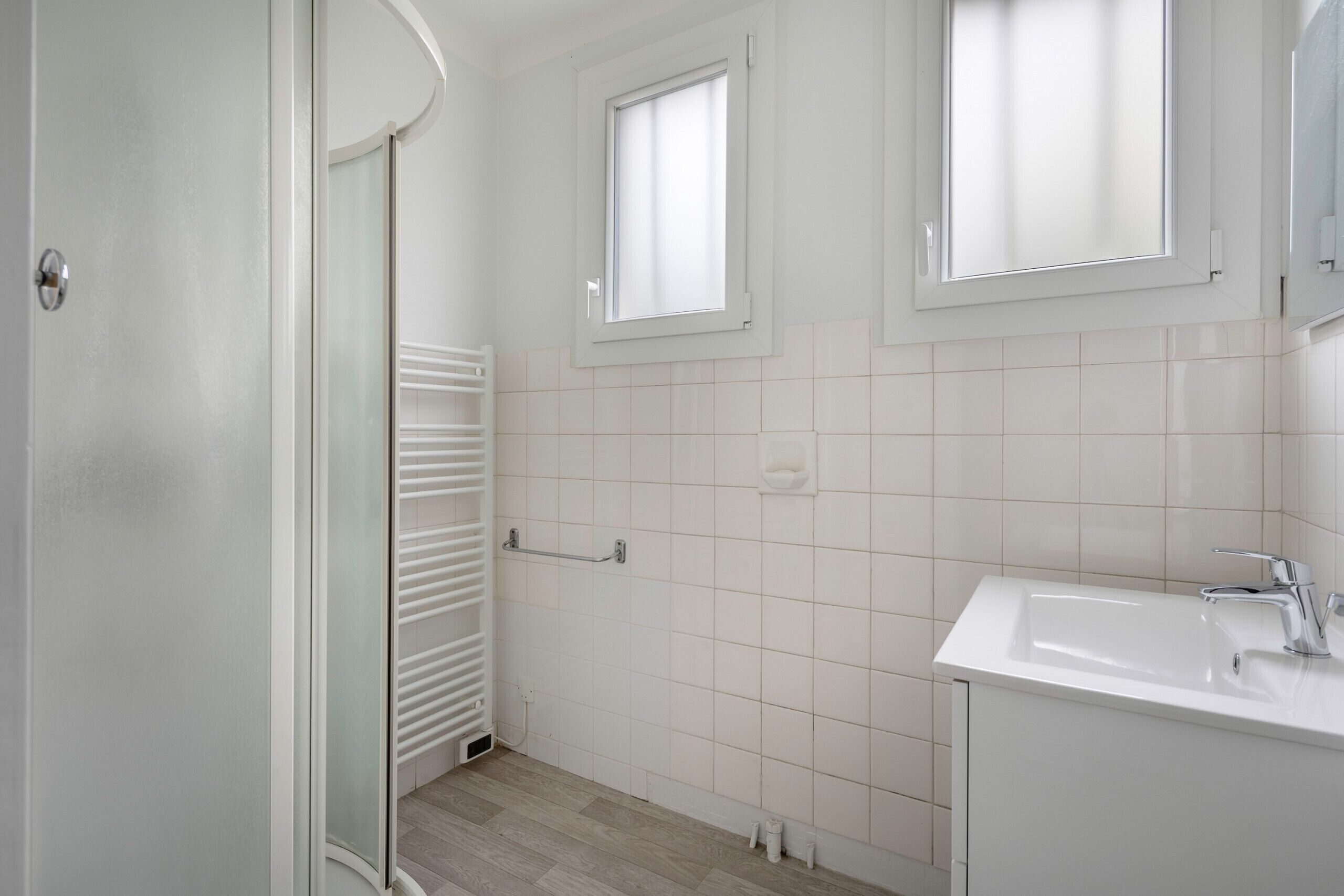 Un baño con un lavamanos blanco, un espejo y una ventana.
