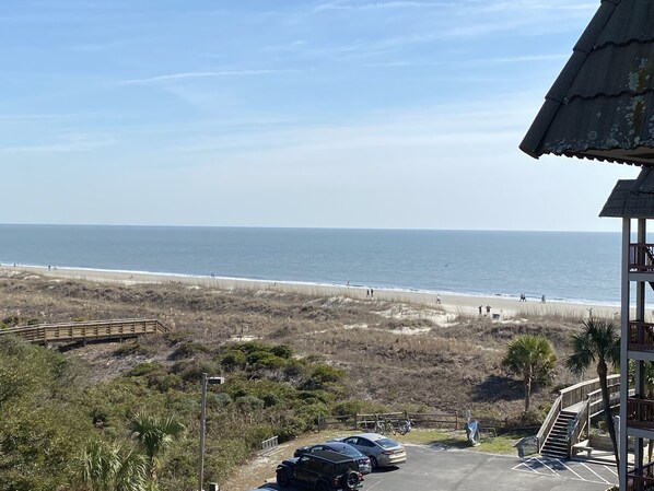 Vista de la playa con un camino de madera que lleva a un estacionamiento.