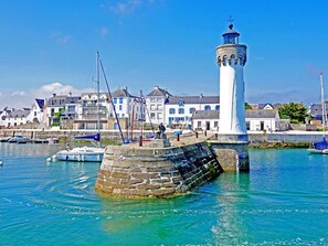 Eine KĂŒstenstadt mit einem markanten Leuchtturm, einer Steinmole und Booten im Wasser.
