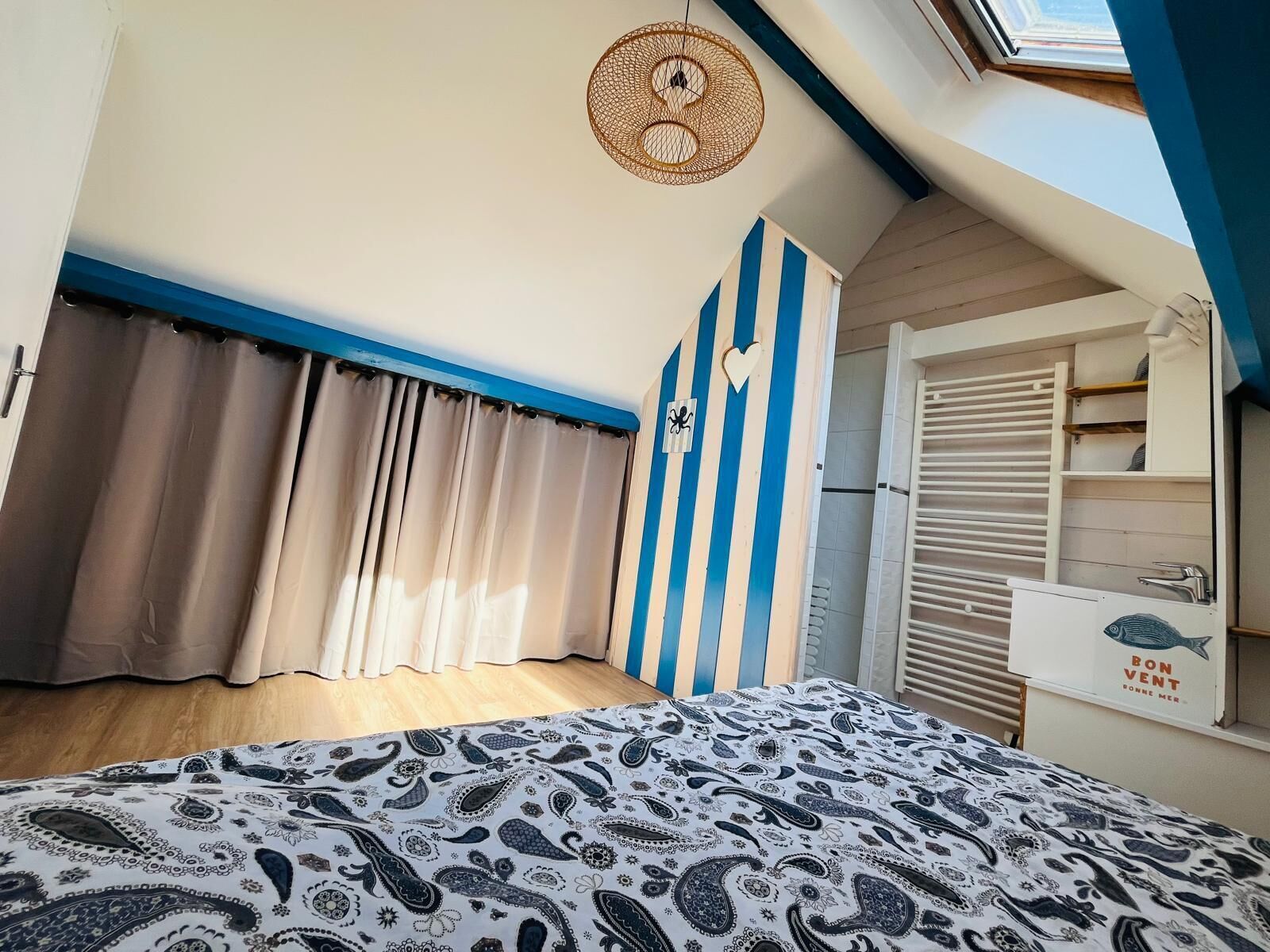 Un dormitorio con cama, cortinas, pared a rayas, ventilador de techo y ventana.