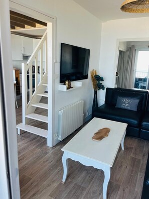 A modern living room with a white coffee table, a black sofa, a mounted TV, and a staircase leading to another room. - Sea view & beach at foot 4 bedrooms ideal for families (Quiberon)