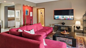 Un soggiorno con un divano rosso, un tavolino, una TV montata a parete e un piccolo angolo da pranzo con tavolo e sedie.
