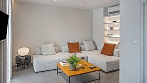 Ein modernes Wohnzimmer mit einer grauen Sofagarnitur, einem Holztisch und einem Beistelltisch mit Lampe und Dekoration.
