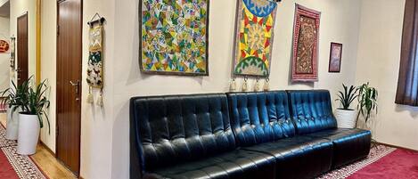 A lobby with a black leather sofa, a red patterned carpet, and various wall art including a large colorful painting and a smaller framed piece.