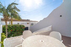 Relax in a serene patio surrounded by lush greenery and a palm tree, with a round table and two comfortable chairs.