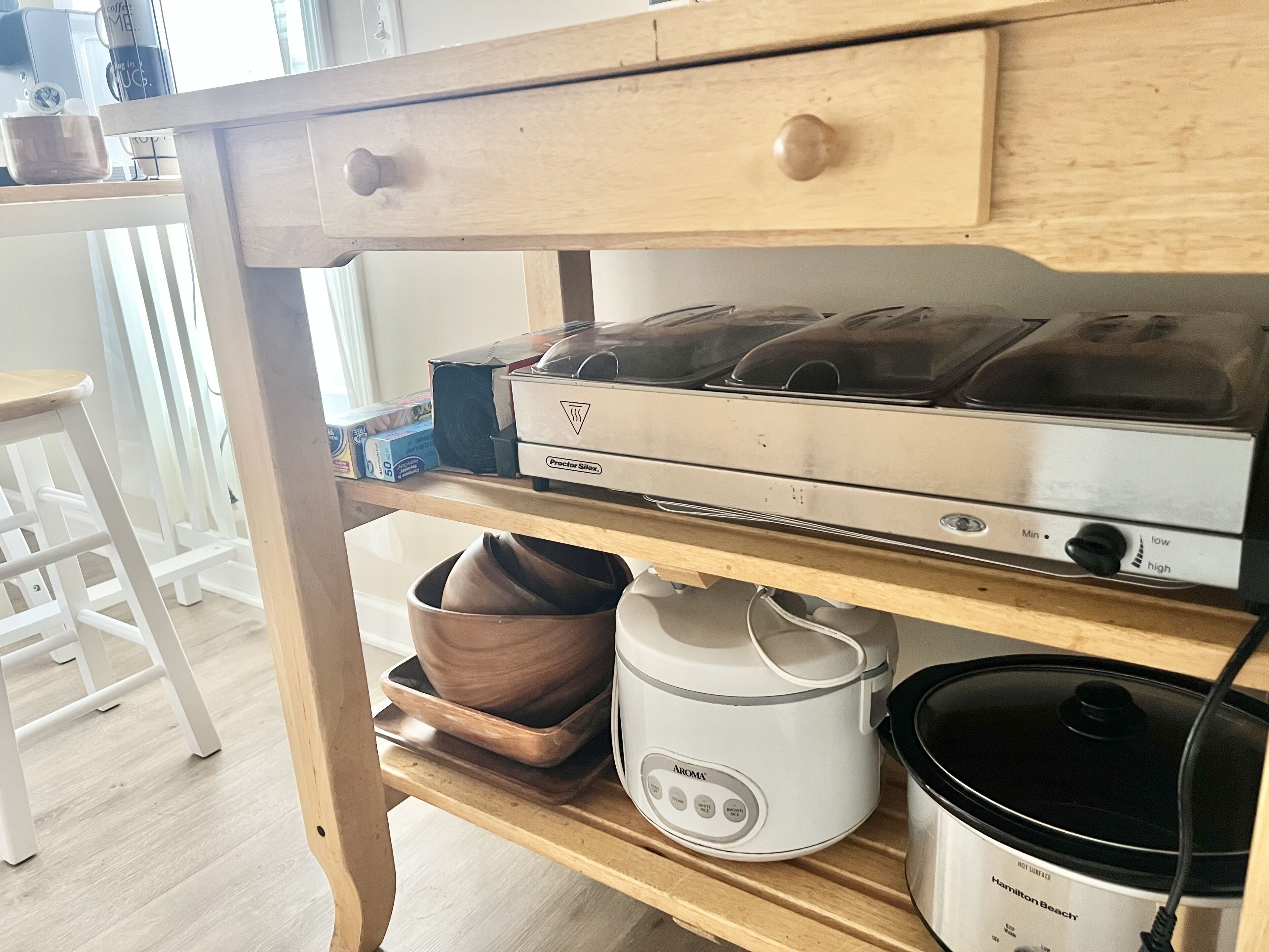 A kitchen with a Proctor Siler stove, a Hamilton Beach slow cooker, and a coffee maker on a wooden shelf.