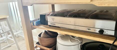 A kitchen with a Proctor Siler stove, a Hamilton Beach slow cooker, and a coffee maker on a wooden shelf.