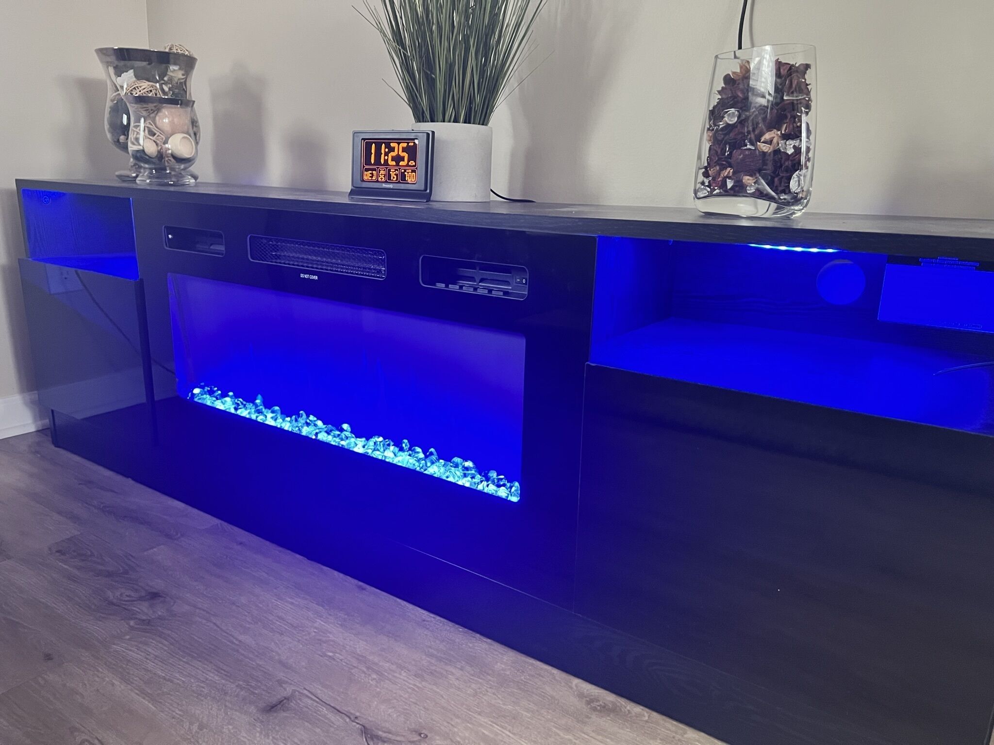 Een aquarium met een digitale klok waarop 11:25 staat, een potplant en decoratieve glazen potten op een houten vloer.