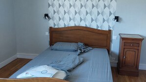 A bedroom with a wooden bed, a geometric-patterned wall, and a small wooden cabinet. - Spacious family home close to the sea (Cayeux-sur-Mer)