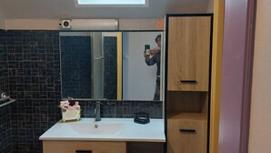 A modern bathroom with a skylight, a large mirror, and a white sink with wooden cabinets. - Spacious family home close to the sea (Cayeux-sur-Mer)