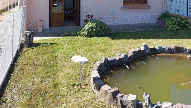 A two-story house with a sloped roof, a small front porch, and a front yard with a stone pond. - Spacious family home close to the sea (Cayeux-sur-Mer)