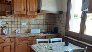 A kitchen with wooden cabinets, a tiled backsplash, a dining table with chairs, and a window. - Spacious family home close to the sea (Cayeux-sur-Mer)