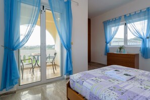 A bedroom with a bed, a wooden dresser, and a balcony with chairs. - Villa Albion (Platanias)
