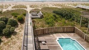 Eine Holzterrasse mit Pool, mit Blick auf einen Strand, der von einem Zaun gesäumt wird und einen uneingeschränkten Blick auf den Ozean bietet.