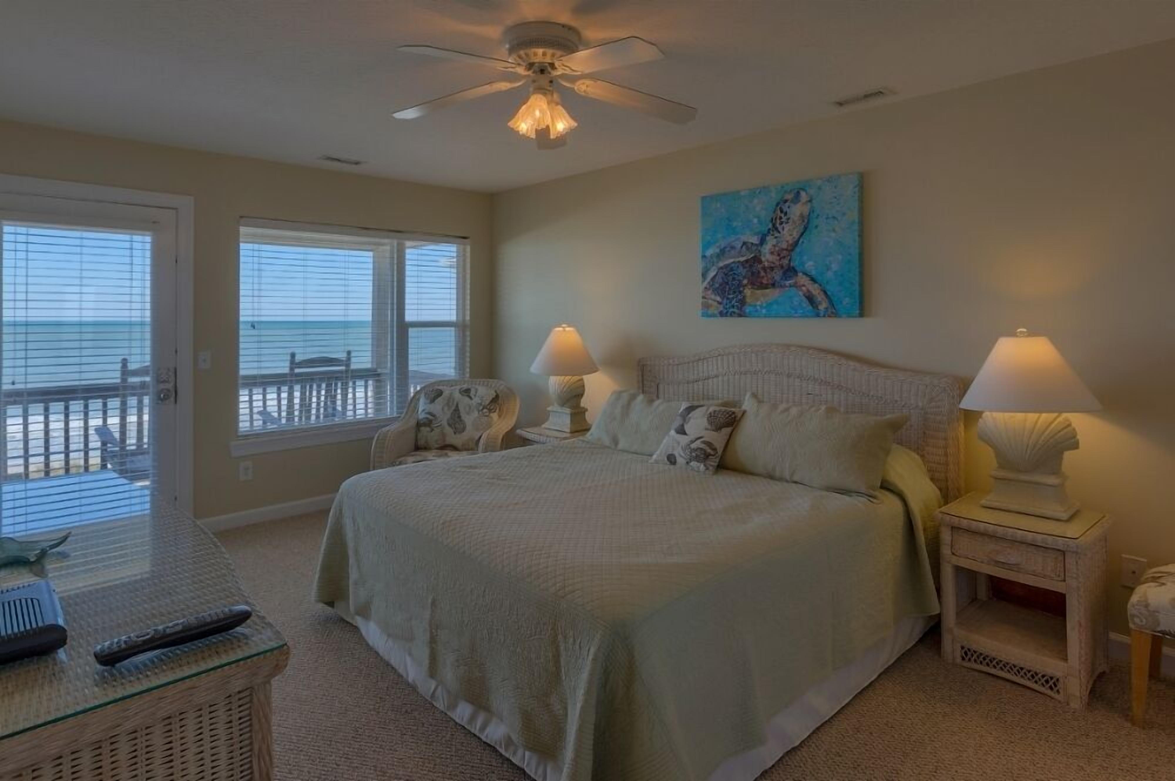 A bedroom with a bed, two bedside tables with lamps, a glass coffee table, a chair, and a painting on the wall.