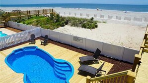 Ein Poolbereich mit Holzterrasse, Liegestühlen und Blick auf den Strand.