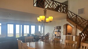 A spacious dining area with a wooden table and chairs, a chandelier, and a staircase with a wooden railing.