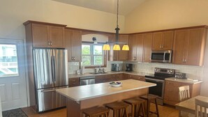 A modern kitchen with wooden cabinets, stainless steel appliances, and a central island with stools.