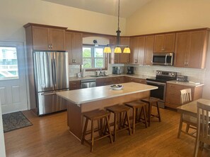 A modern kitchen with wooden cabinets, stainless steel appliances, and a central island with stools. - Hobbs Realty - The "Sandlapper" is an oceanfront home with two living areas and handicap ramps. (Holden Beach)