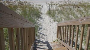 A wooden staircase leading to a beach with sand and sparse vegetation.