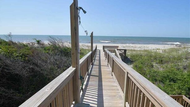 A wooden boardwalk leading to a beach with a clear view of the ocean.