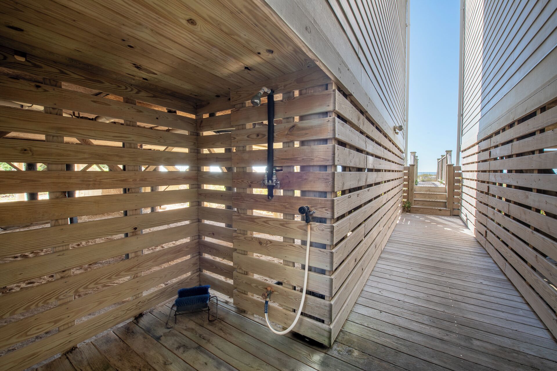 Una sauna de madera con techo y paredes de listones, una terraza de madera y vista a la playa.