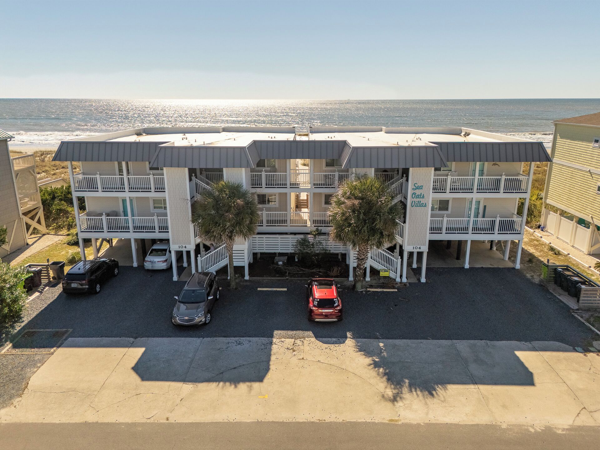 Un hôtel situé en bord de mer, avec une structure à deux étages, des balcons et un espace de stationnement.