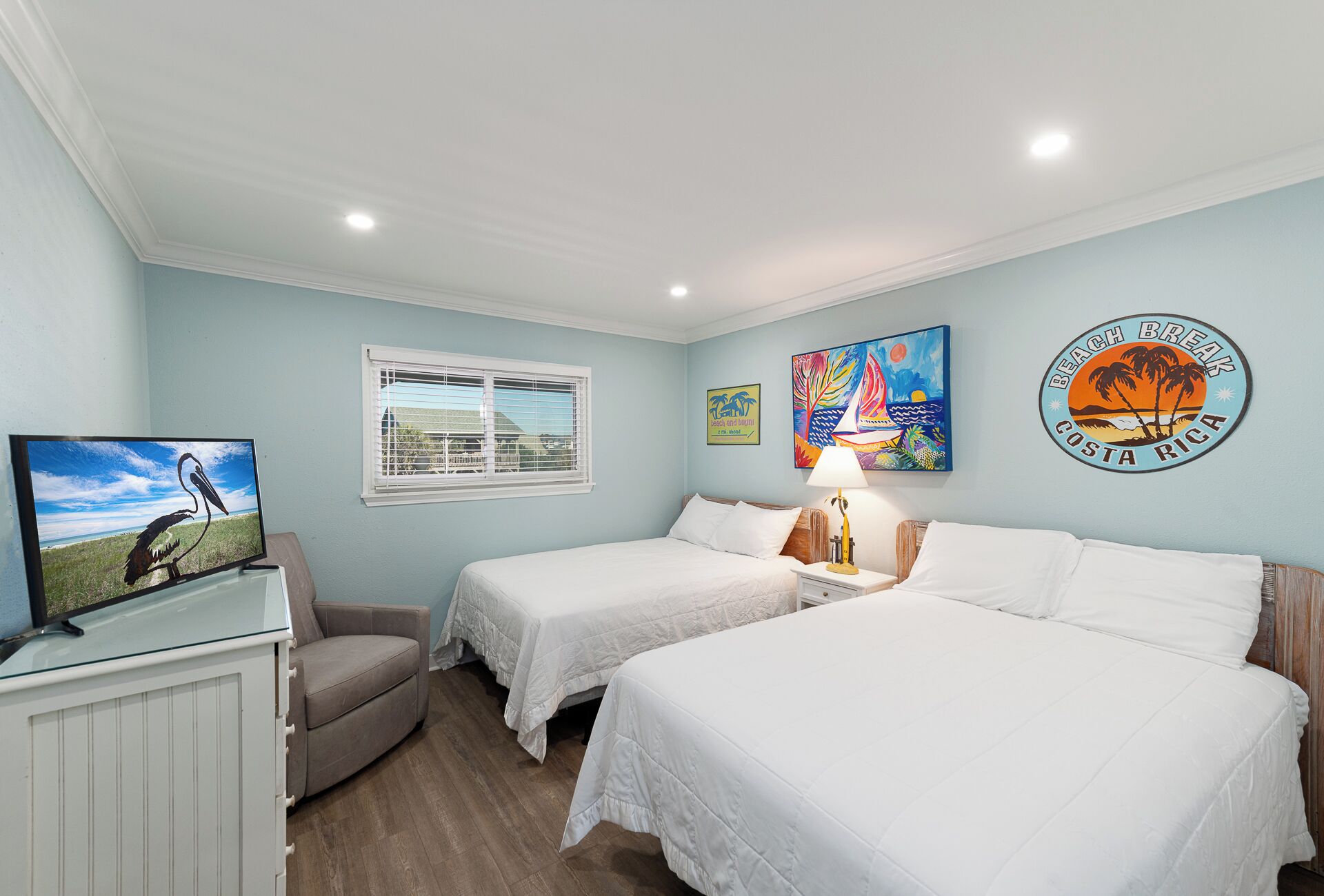Un dormitorio con dos camas, televisión, una silla y obras de arte en las paredes.