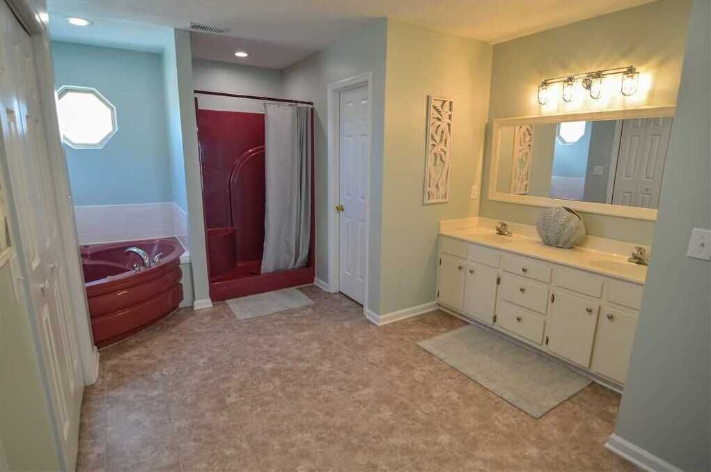 A bathroom with a bathtub, shower, vanity, and a large mirror with lights.