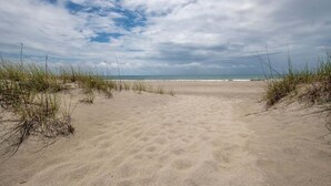 Une plage de sable avec des dunes et de l’herbe au premier plan, qui s’étend jusqu’à l’océan.