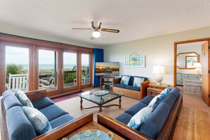 A spacious living room with a large window overlooking the ocean, a ceiling fan, and a television.
