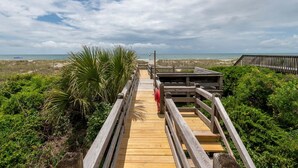Une promenade en bois qui mène à une plage, d’où l’on peut admirer l’océan et un ciel nuageux.