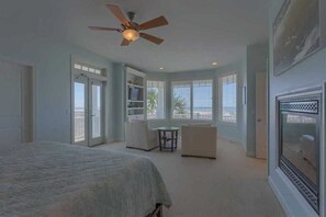 Un dormitorio con cama, ventilador de techo, televisor, zona de estar con mesa y ventanas amplias que ofrecen vistas.