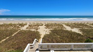 Vista de una playa con una terraza de madera y barandal blanco.