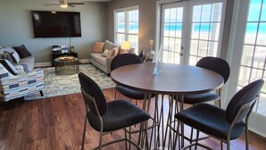 Una sala de estar con un sofá, una mesa de centro y un televisor. Hay un ventanal con vista a la playa.