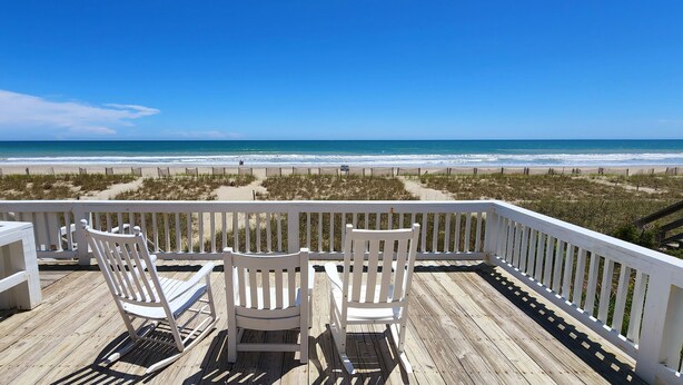 Una terraza de madera con dos sillas Adirondack blancas mirando hacia la playa.