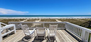 A wooden deck with two white Adirondack chairs facing a beach. - Hobbs Realty - “Signals” | Oceanfront Pet-Friendly Home w/ Private Pool & Beds Made (Holden Beach)