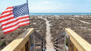 A wooden boardwalk leading to a beach with an American flag.