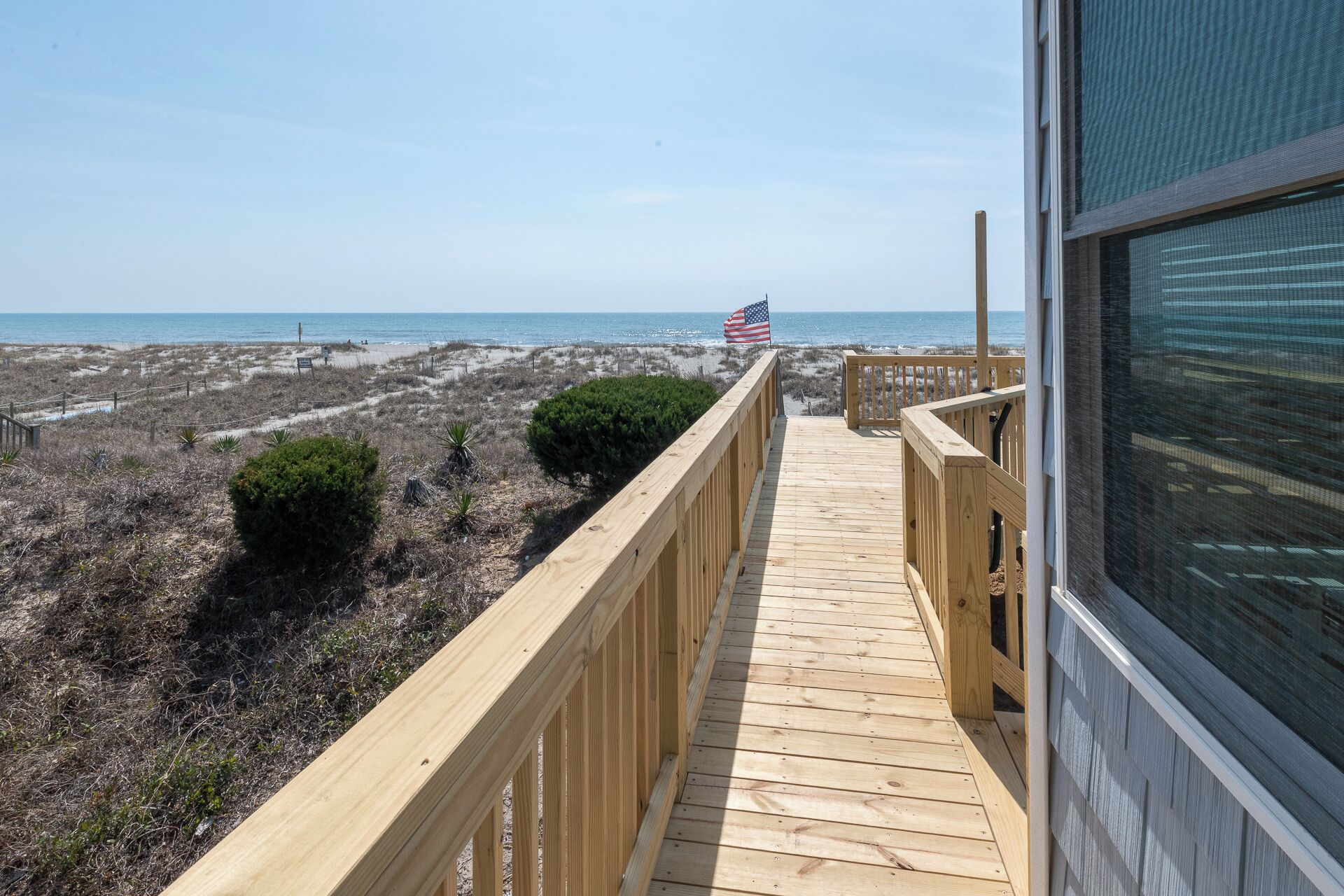A wooden deck leading to a beach with an American flag, overlooking the ocean.
