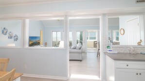 A spacious living area with a large window, a gray sofa, and a kitchen area with white cabinets and a countertop.