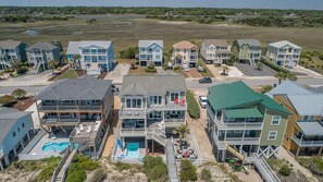 Residential homes with balconies and decks sit elevated on stilts, offering ocean views and access to a swimming pool.