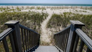 Una escalera de madera que lleva a una playa, con una valla de madera y dunas de arena.