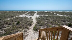 Un sentier bordant la plage et menant à l’océan, avec une terrasse en bois au premier plan.