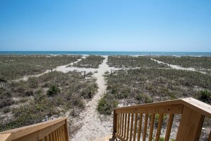 Un sentiero sulla spiaggia che conduce verso l'oceano, con un pontile di legno in primo piano.